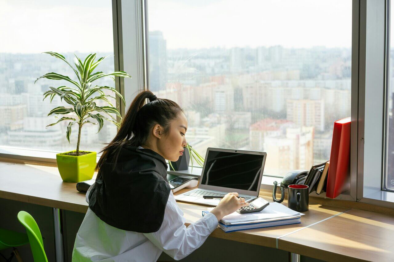 Young female Asian woman sitting at window desk on laptop