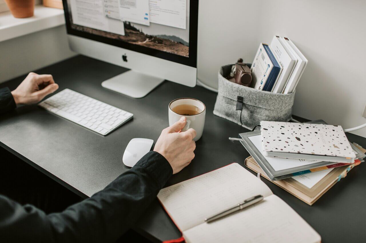 Man sitting at desk with notepad, computer screen and cup of coffee working on his project management tasks