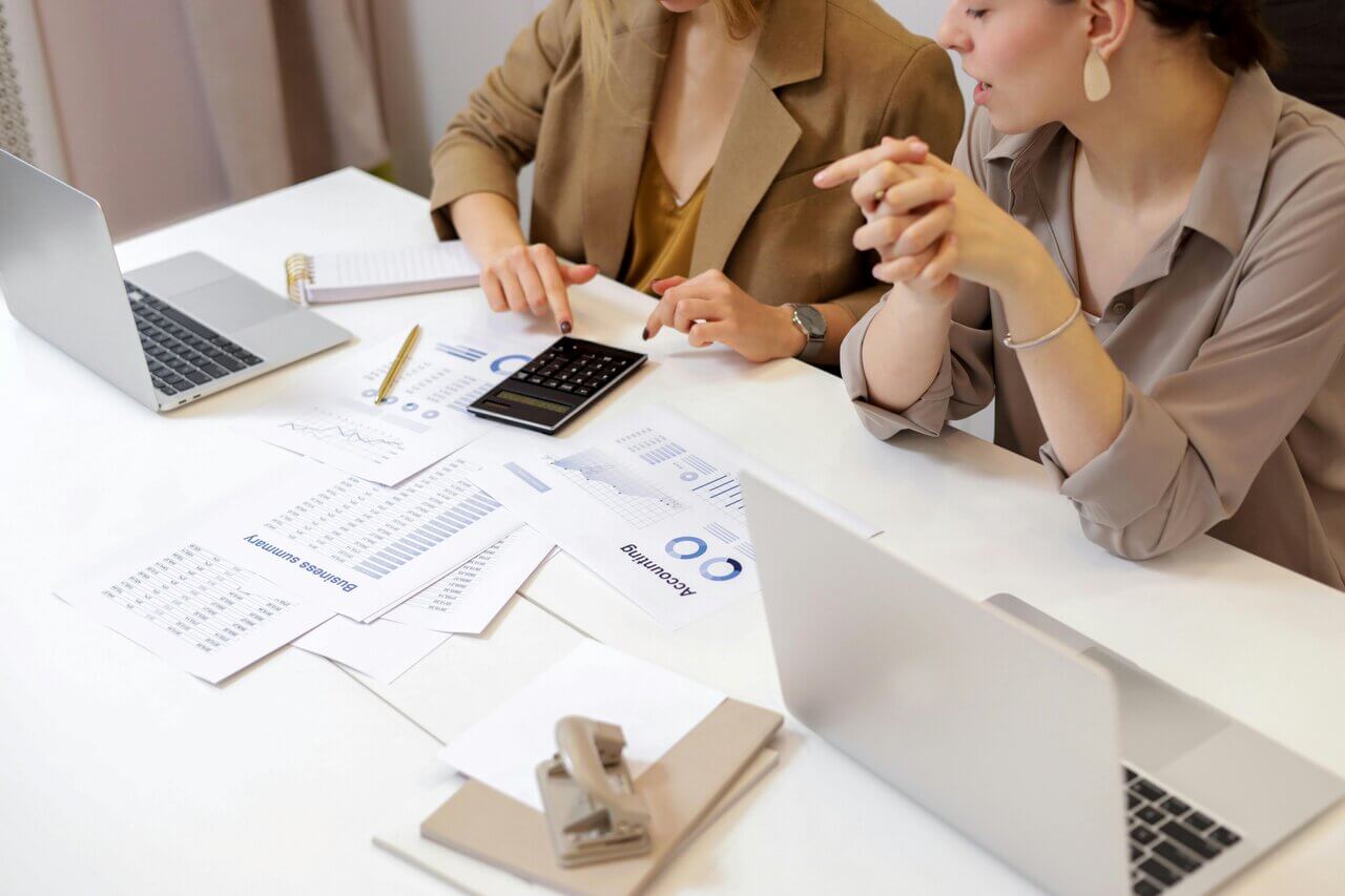 Two female bookkeepers sitting at a desk discussing AAT qualification costs
